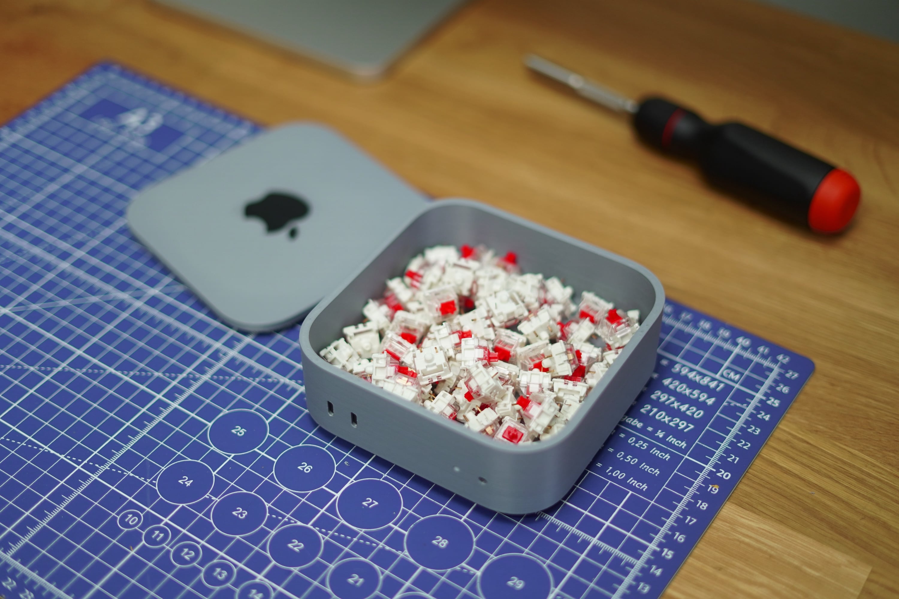 A 3D printed Mac mini with a removable top that is holding red keyboard switches, with a screwdriver visible in the background