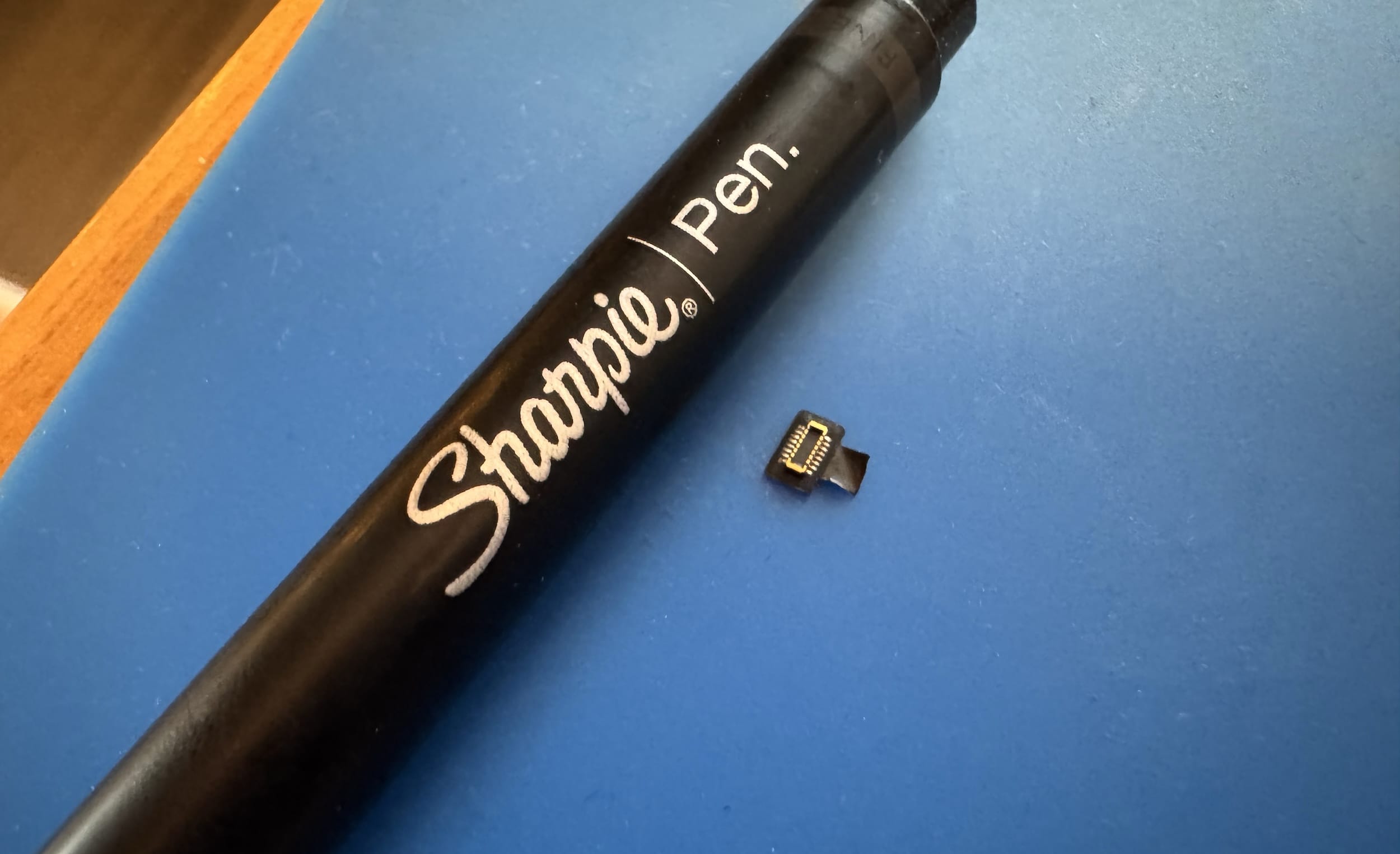 Torn off Touch ID sensor sitting beside a Sharpie pen for scale